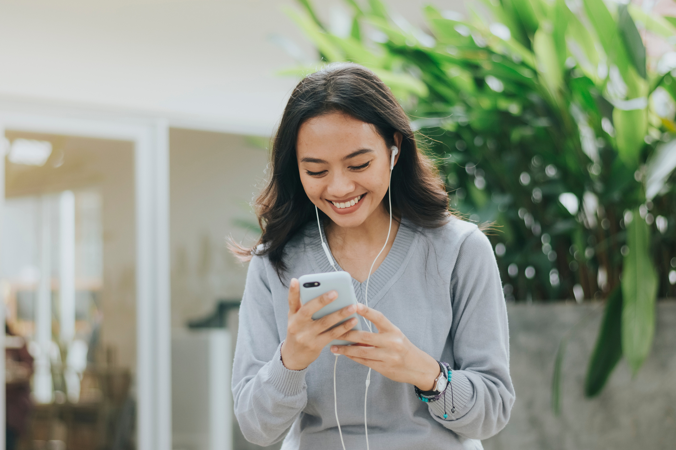 Smiling Woman in Earphones Using Her Smartphone Outdoors